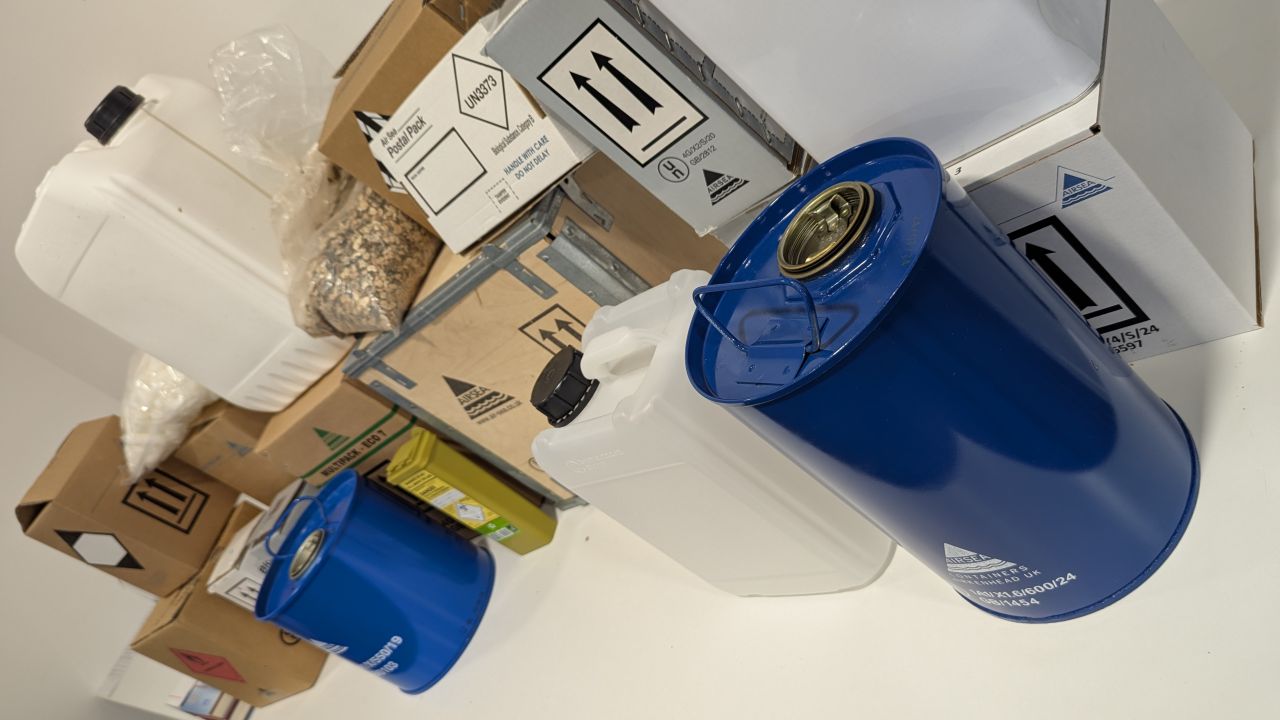 Dangerous goods shipment with blue drums, white containers, and hazmat-labeled cardboard boxes